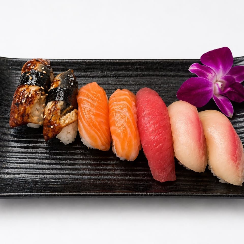 Assortment of nigiri sushi, including eel, salmon, tuna, and white fish, on a black plate with an orchid.